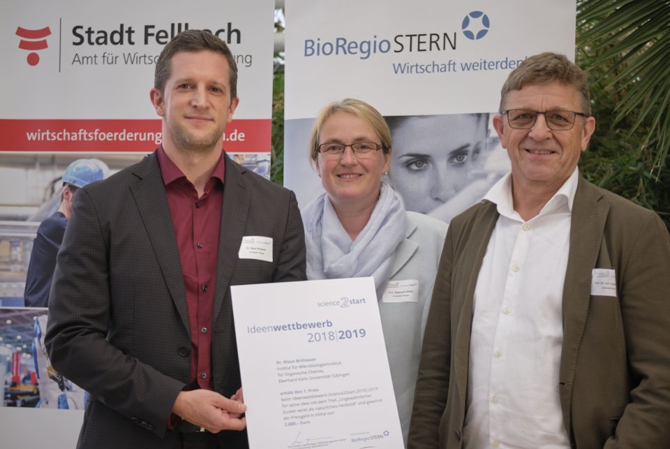 3 Personen stehen für ein Bild aufgereiht nebeneinander und halten die Urkunde über die Erstplatzierung in die Kamera.