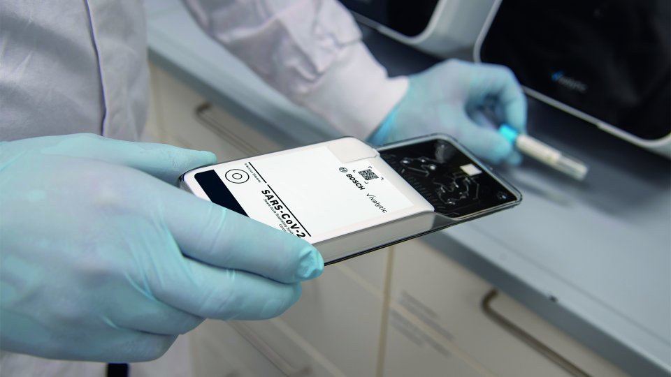 Hände in hellblauen Handschuhen halten den Analyzer mit Kartusche