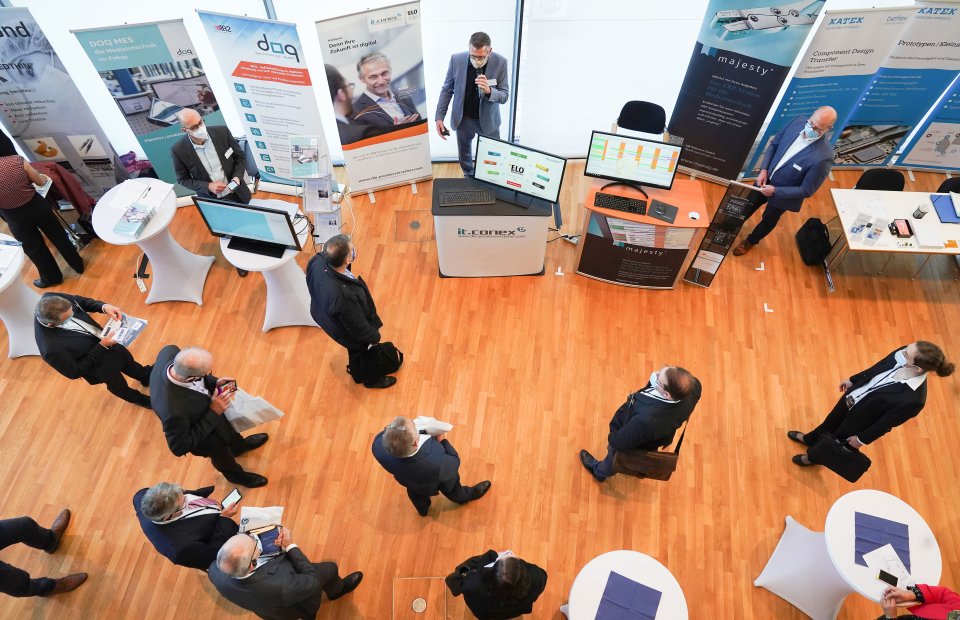 Mehrere Personen laufen durch eine Ausstellung in welcher verschiedene Stände aufgebaut sind.