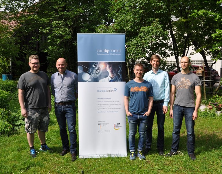 5 Männer stehen für ein Gruppenbild vor einem Roll-up in einer Wiese.
