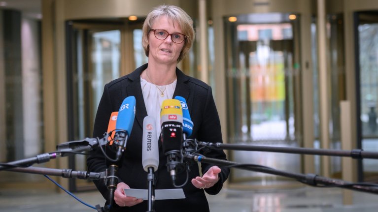 Bundesforschungsministerin Anja Karliczek steht in einem großen Raum. Vor ihr befinden sich fünf Mikrofone um ihr Statement aufzunehmen.