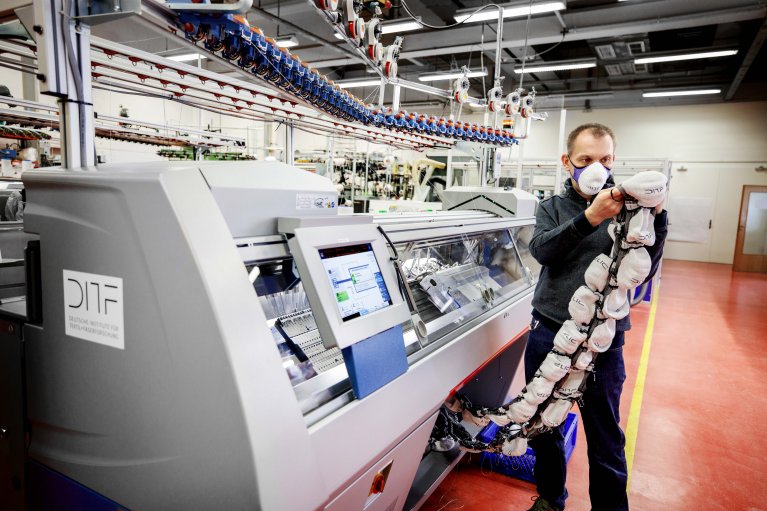 Ein Mitarbeiter zieht eine Kette an gestrickten Masken aus einer Maschine.