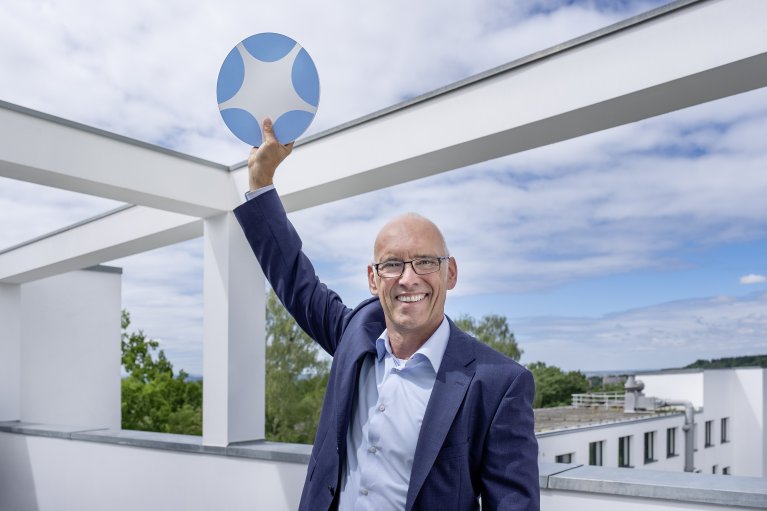 Ein Mann im Anzug steht auf einem Gebäude und hält das BioRegioSTERN Logo in die Höhe.