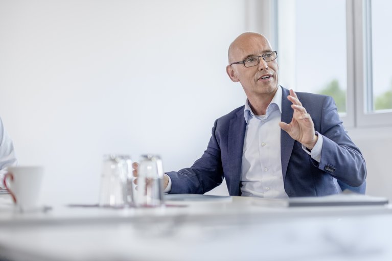 Dr. Steffen Hüttner sits in a suit at a conference table and speaks.