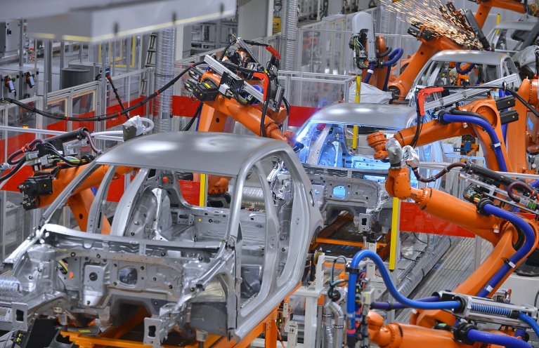 Eine weiße Karosserie eines Autos wird von orangefarbenen Robotern bearbeitet