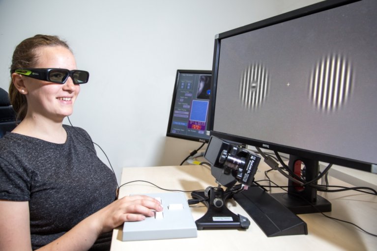 Eine Frau sitzt mit einer speziellen Brille vor einem Bildschirm.