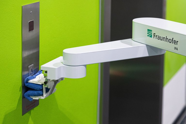 Nahaufnahme des armähnlichen Bauteils des Roboters bei der Desinfektion von Aufzugknöpfen in einem hellgrünen Aufzug.