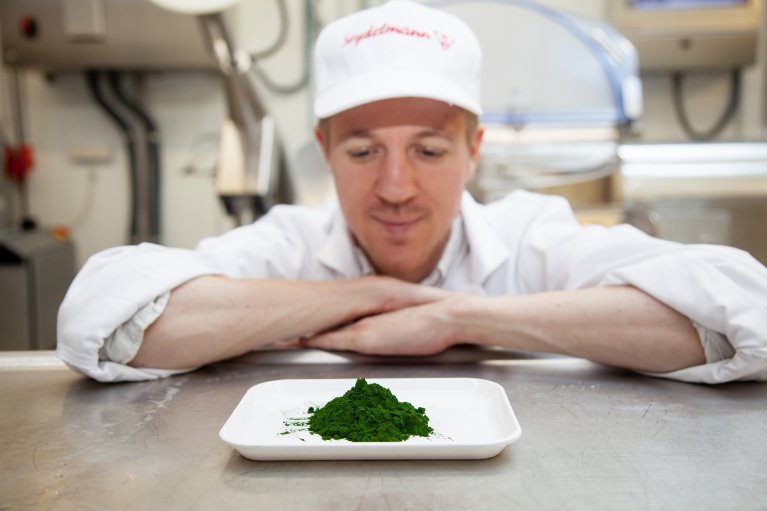 Ein Mann betrachtet ein Häufchen grüner Algen auf einem weißen Teller.