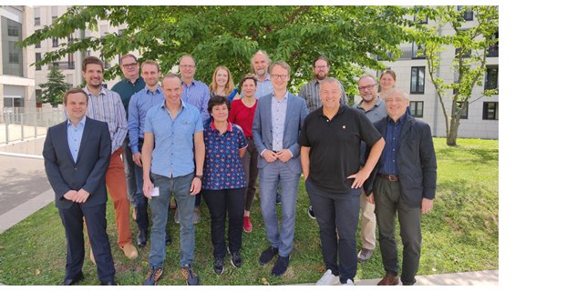 Gruppenfoto des Klima.Neutral.Digital Projektteams & Dr. Arthur Korus vom Projektträger „Deutsches Zentrum für Luft- und Raumfahrt e. V. (DLR). Die Gruppe steht im Freien. Im Hintergrund sind Gebäude und Bäume zu sehen.
