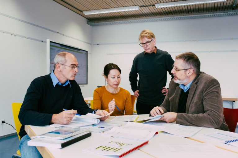Mehrere Personen stehen und sitzen an einem Runden Tisch