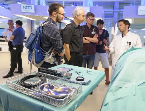 Several people discuss with each other. In the foreground are several medical devices and objects.