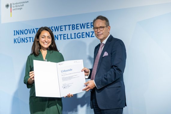 Claudia Salwiczek-Majonek steht neben Staatssekretär Dr. Ulrich Nussbaum. Dieser überreicht die Urkunde.