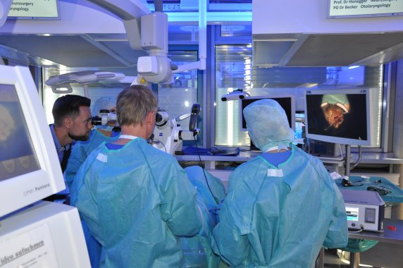 Mehrere Ärzte stehen mit grüner OP und sehen durch ein Mikroskop.
