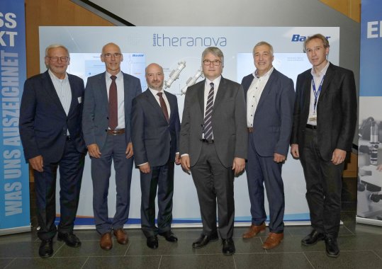 6 Männer stehen für ein Gruppenbild nebeneinander vor einem Roll-up der Baxter-Gruppe.