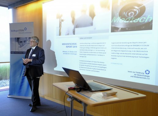 Dr. Klaus Eichenberg, Geschäftsführer der BioRegio STERN Management GmbH begrüßt die Teilnehmer. Er steht vor einer Leinwand und wendet sich zum Publikum.