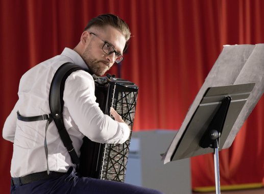 A man sits on a chair and plays the accordion.