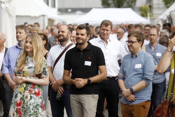 Viele Personen stehen zur Bühne gerichtet und hören zu.