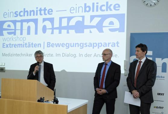 Three people are standing in front of a beamer, one person talking in a microphone